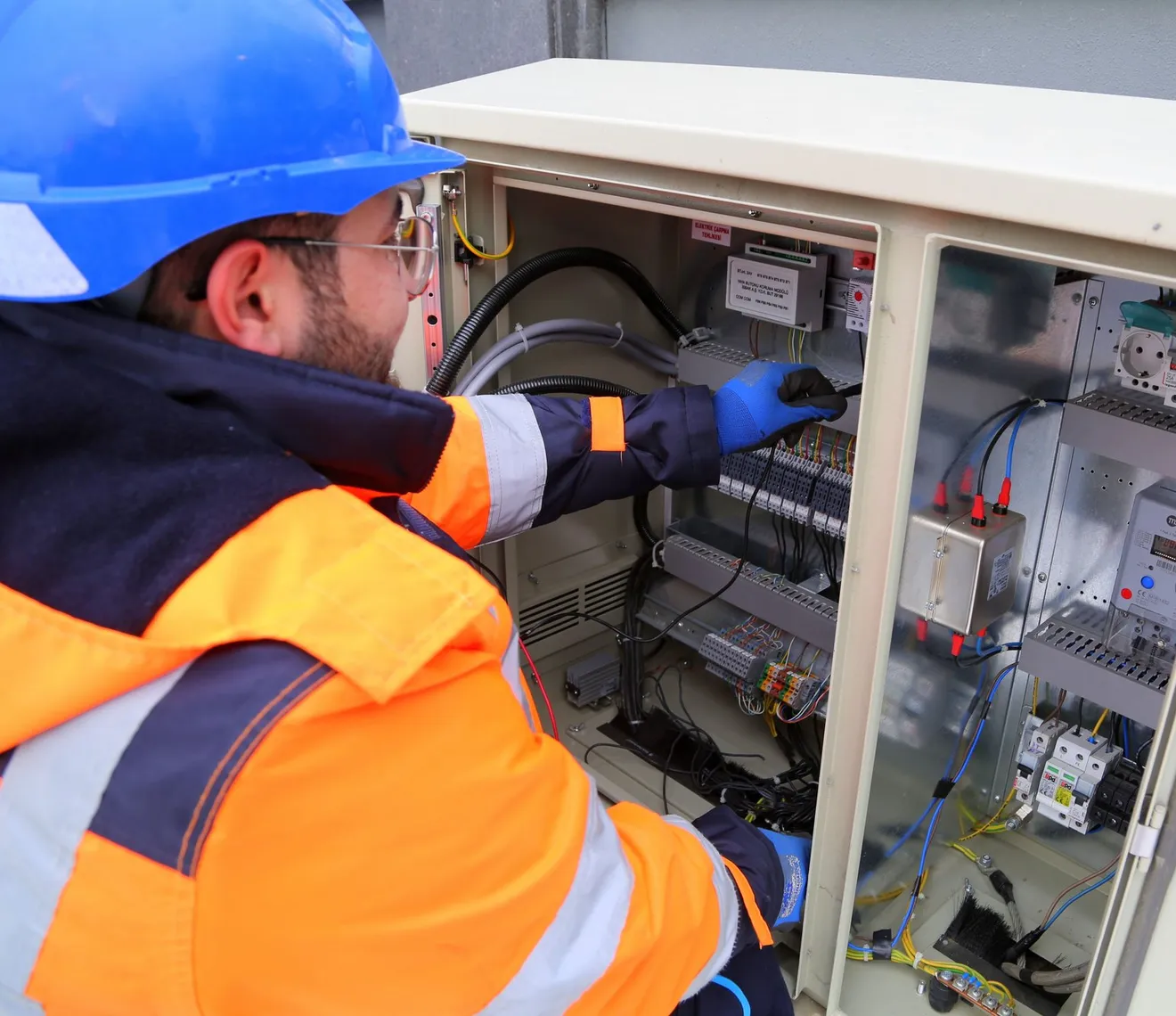Elektryk w kasku i kamizelce odblaskowej wykonujący prace przy otwartej rozdzielnicy elektrycznej